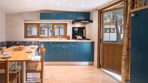 Una cocina con armarios azules, una mesa de comedor de madera con sillas, una estufa y una ventana con vistas a árboles.