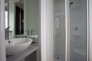 A modern bathroom with a white sink, a mirror, and a glass-enclosed shower.