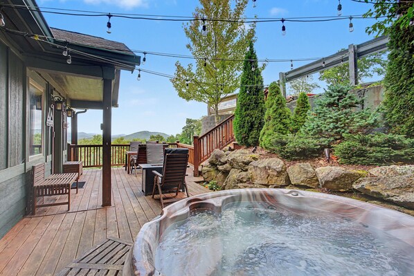 A wooden deck with outdoor furniture, a hot tub, and a stone wall. - Chalet with sweeping mountain views near Blowing Rock and Boone (Blowing Rock)
