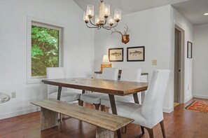 Un coin repas avec une table et des chaises en bois, un banc, un lustre et des tableaux représentant des poissons, accrochés au mur.