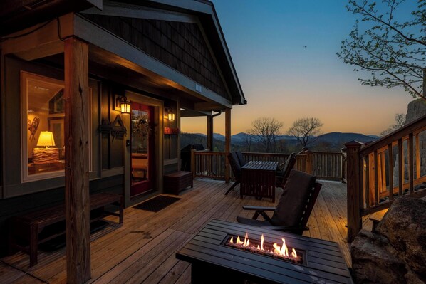 Une terrasse en bois avec un foyer, des sièges d’extérieur et une vue sur les montagnes.