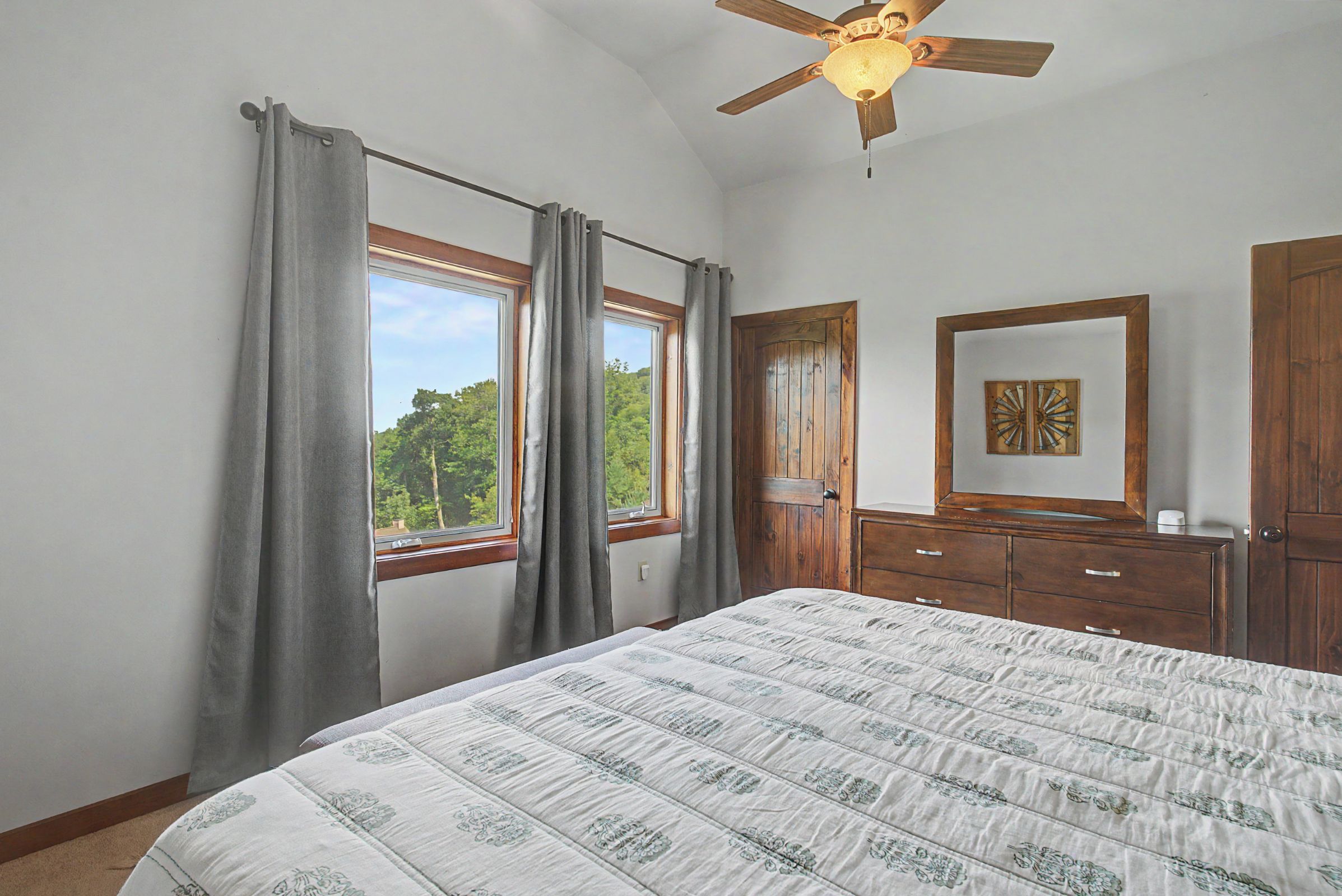 Un dormitorio con cama, ventilador de techo, cómoda, espejo y ventana con cortinas.