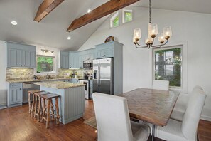 Una cocina moderna con una isla central, electrodomésticos de acero inoxidable y un comedor con mesa de madera y sillas blancas.