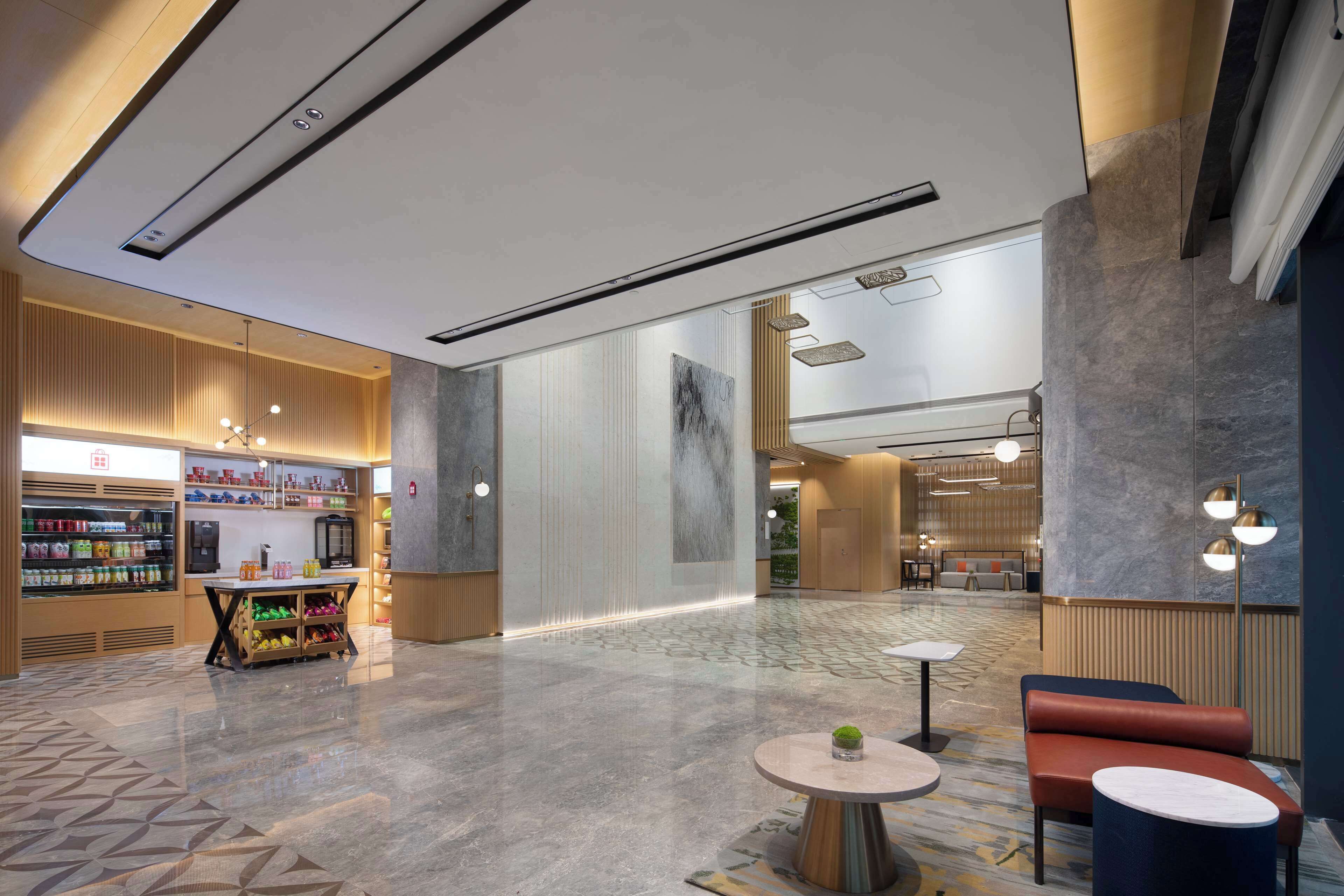 Un hall d’hôtel moderne comprenant un comptoir d’accueil, un espace salon et un bar où l’on peut prendre une collation.