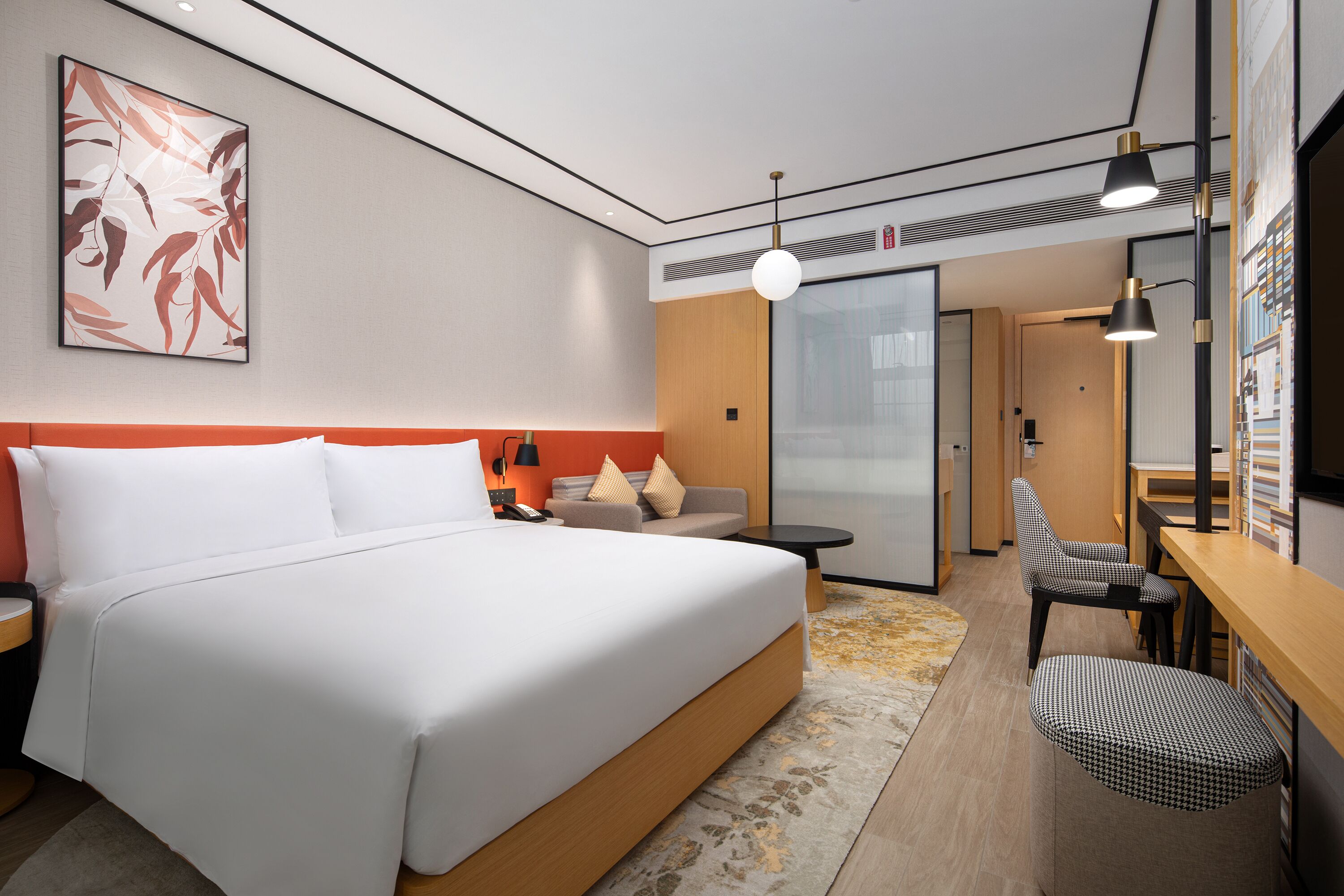 A modern hotel room with a large bed, a sofa, a desk, and a chair. There is a painting on the wall and a window with a view.