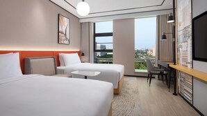 Une chambre d’hôtel avec deux lits, un bureau, une chaise, une télévision et une grande fenêtre donnant sur la ville.