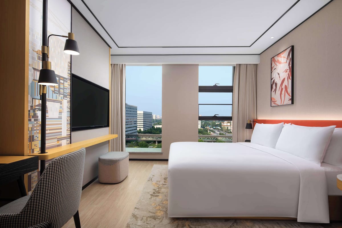 Une chambre d’hôtel moderne dotée d’un grand lit, d’un bureau avec une chaise, d’un téléviseur à écran plat et offrant une vue sur la ville par la fenêtre.