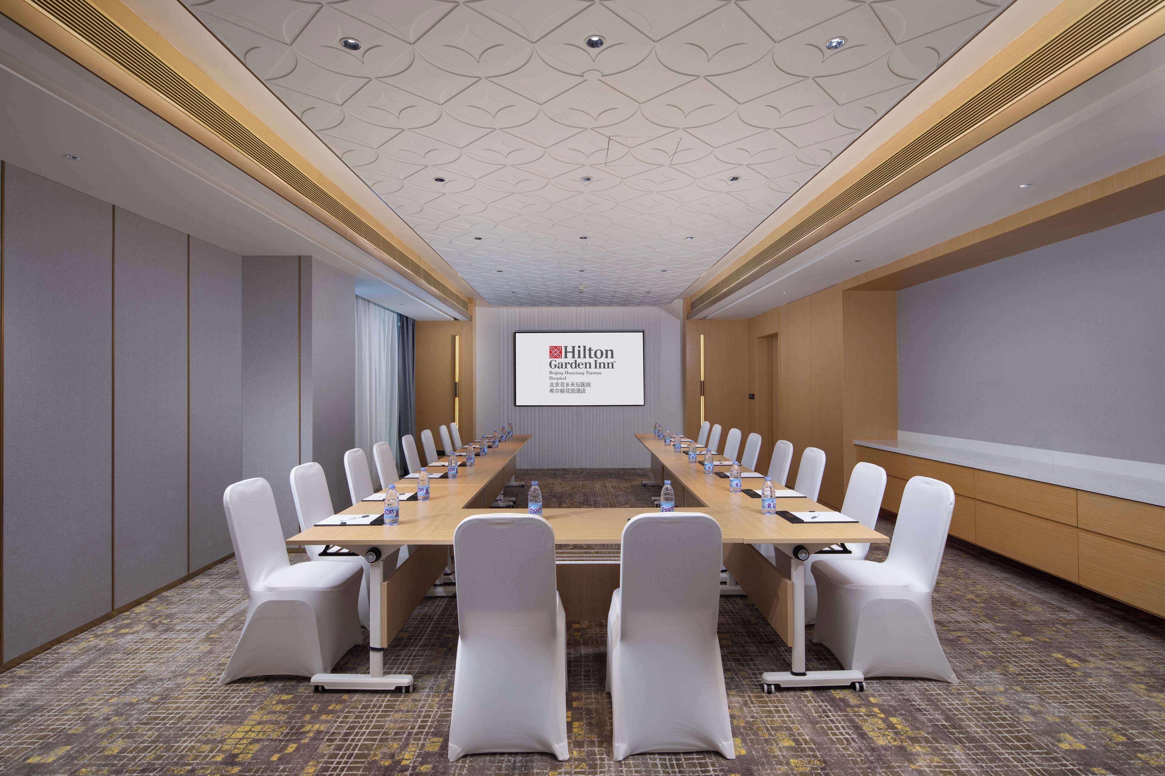 A conference room with a long table, white chairs, and a projector screen displaying the Hilton Garden Inn logo.