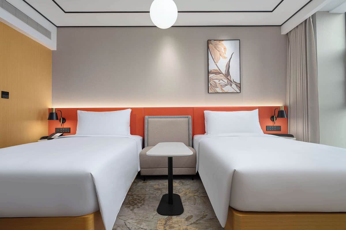 Une chambre d’hôtel avec deux lits, une petite table et un tableau au mur.