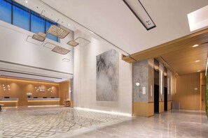 Un hall d’entrée spacieux avec un comptoir de réception, une grande œuvre d’art abstraite murale et un plafond haut orné de luminaires suspendus.