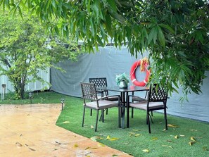 Eine Terrasse im Freien mit Tisch und Stühlen, umgeben von Kunstrasen und einem Pflasterweg.