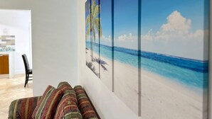 A living room with a sofa and a large beach-themed painting on the wall. - Relaxing Retreat 2BR Oasis w/ Pool and Outdoor BBQ (Pembroke Pines)