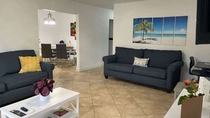 A modern living room with two dark sofas, a white coffee table, and a dining area in the background. - Relaxing Retreat 2BR Oasis w/ Pool and Outdoor BBQ (Pembroke Pines)