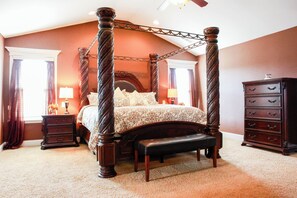 Four-poster bed with nightstands and a dresser, set against a warm backdrop.
