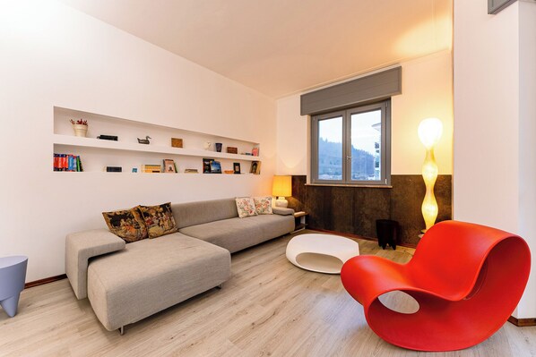 A modern living room with a grey sofa, a red chair, and a bookshelf filled with books and decorative items.