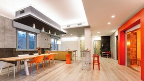 Una cocina moderna con comedor, que presenta una mesa de madera y sillas naranjas, una isla de cocina y una pared de acento roja.