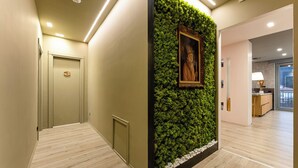 Un pasillo con un muro vertical de jardín verde, un retrato enmarcado y una puerta de madera.