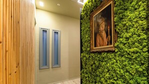 Un pasillo con panel de madera, dos ventanas con marcos azules y una pared cubierta de musgo verde con un retrato enmarcado.