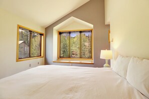 Ein Schlafzimmer mit einem großen Bett, zwei Fenstern und einer Lampe.
