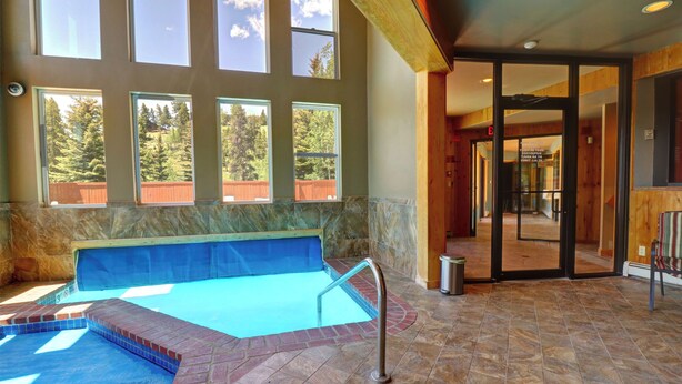 A swimming pool with a view of trees through large windows, a stone-tiled floor, and a wooden deck area. - Beautiful Views, Awesome Amenities, 195 Eastridge (Dillon)