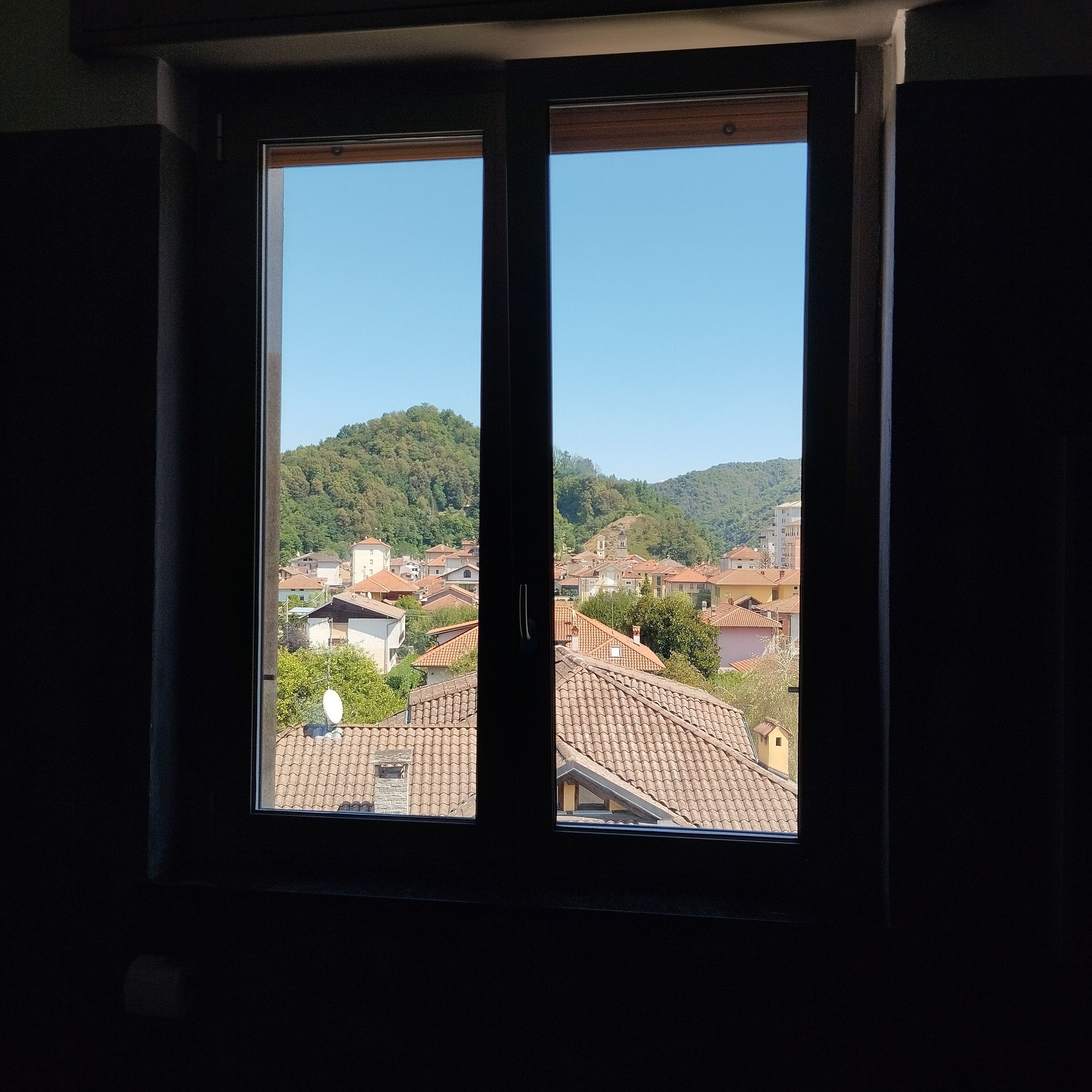 A window with a view of a residential area with houses and a hill in the background.