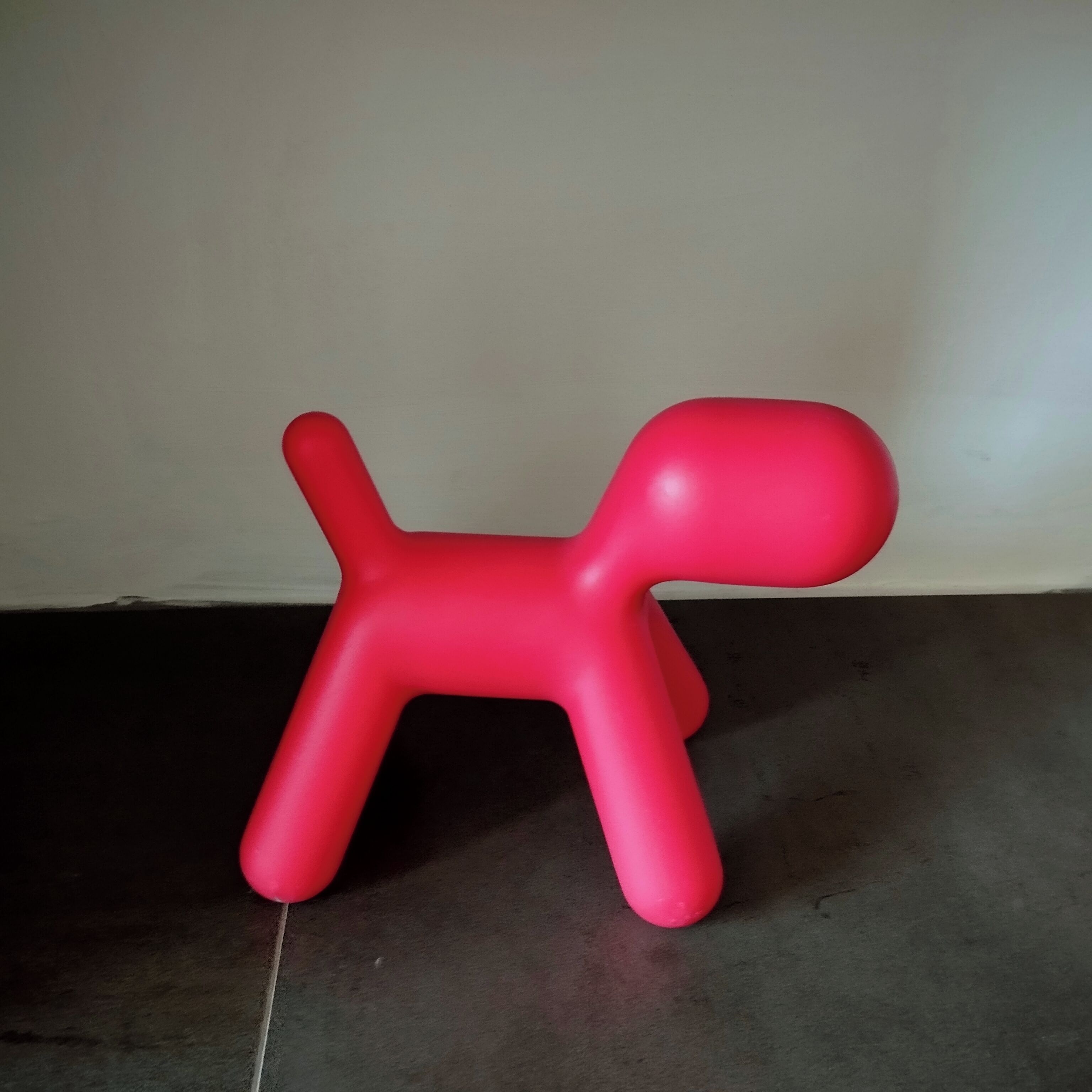 A red plastic dog-shaped object on a dark floor against a plain wall.