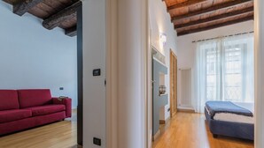 Un apartamento moderno con sofá rojo, cama, suelo de madera y un radiador visible.