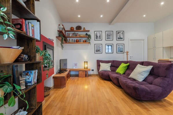 A living room with a wooden floor, a purple sofa, a bookshelf, and a fireplace. - La Corte by Wonderful Italy (Turin)