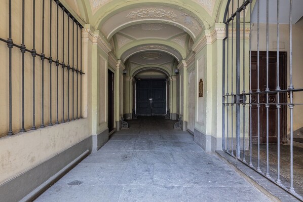 A corridor with a metal gate on the right, a dark door at the end, and a light-colored wall with decorative molding. - La Corte by Wonderful Italy (Turin)