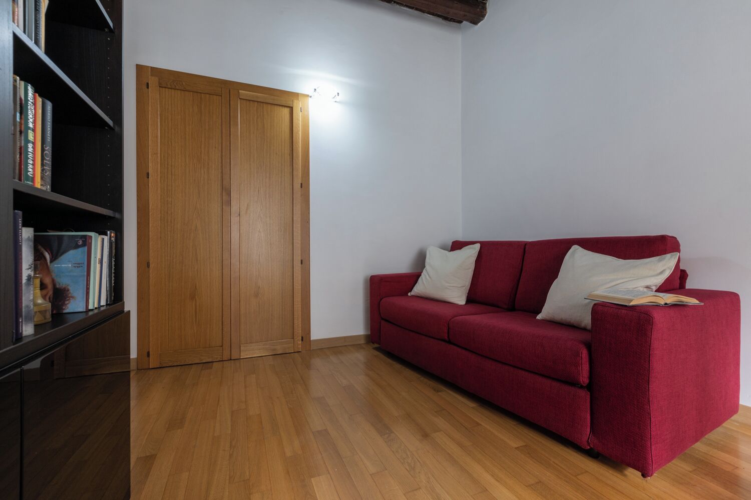 A room with a red sofa, a wooden wardrobe, and a bookshelf with books.