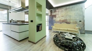 A modern kitchen with white cabinets and a built-in oven. There is a green accent wall and a vintage-style sofa in the living area.