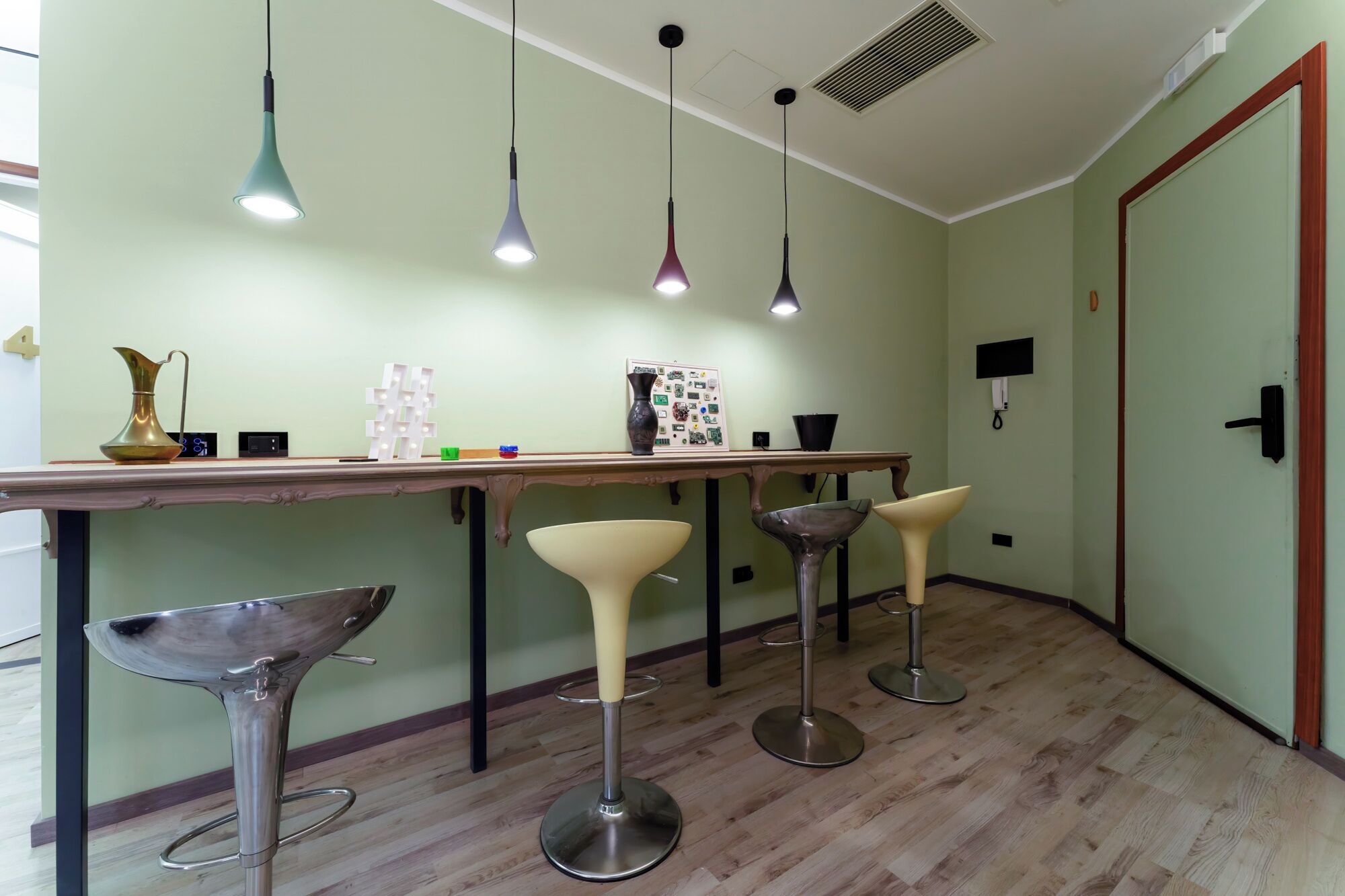 A modern kitchen with a wooden countertop, bar stools, pendant lights, and a decorative vase.