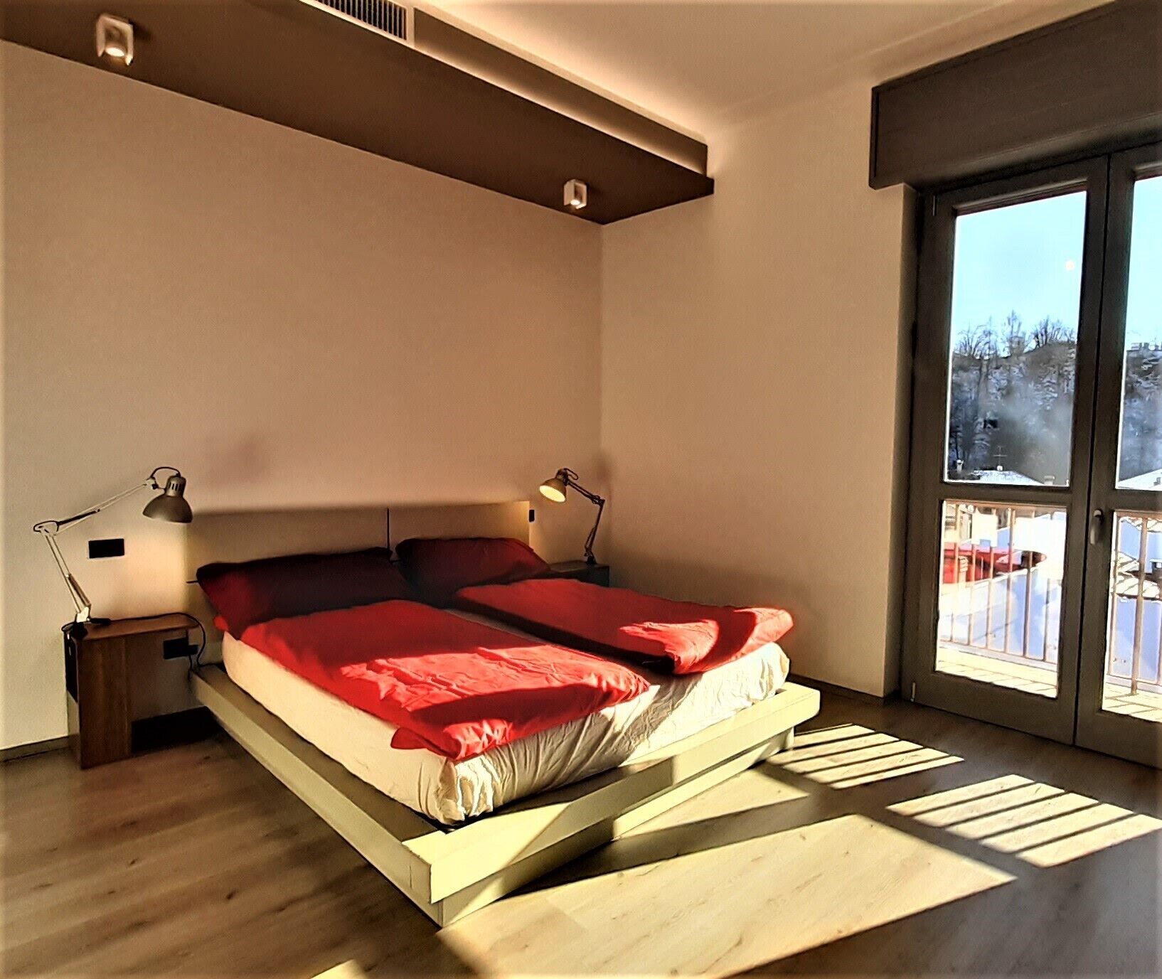 Un dormitorio moderno con cama, lámparas de noche y un ventanal con vistas a un paisaje nevado.