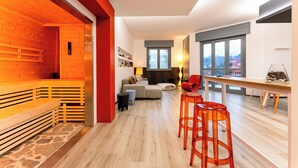 A modern living room with a wooden bench, a sofa, and a dining area with stools. - Camere CA + Millo - Camera 3 (Crevacuore)