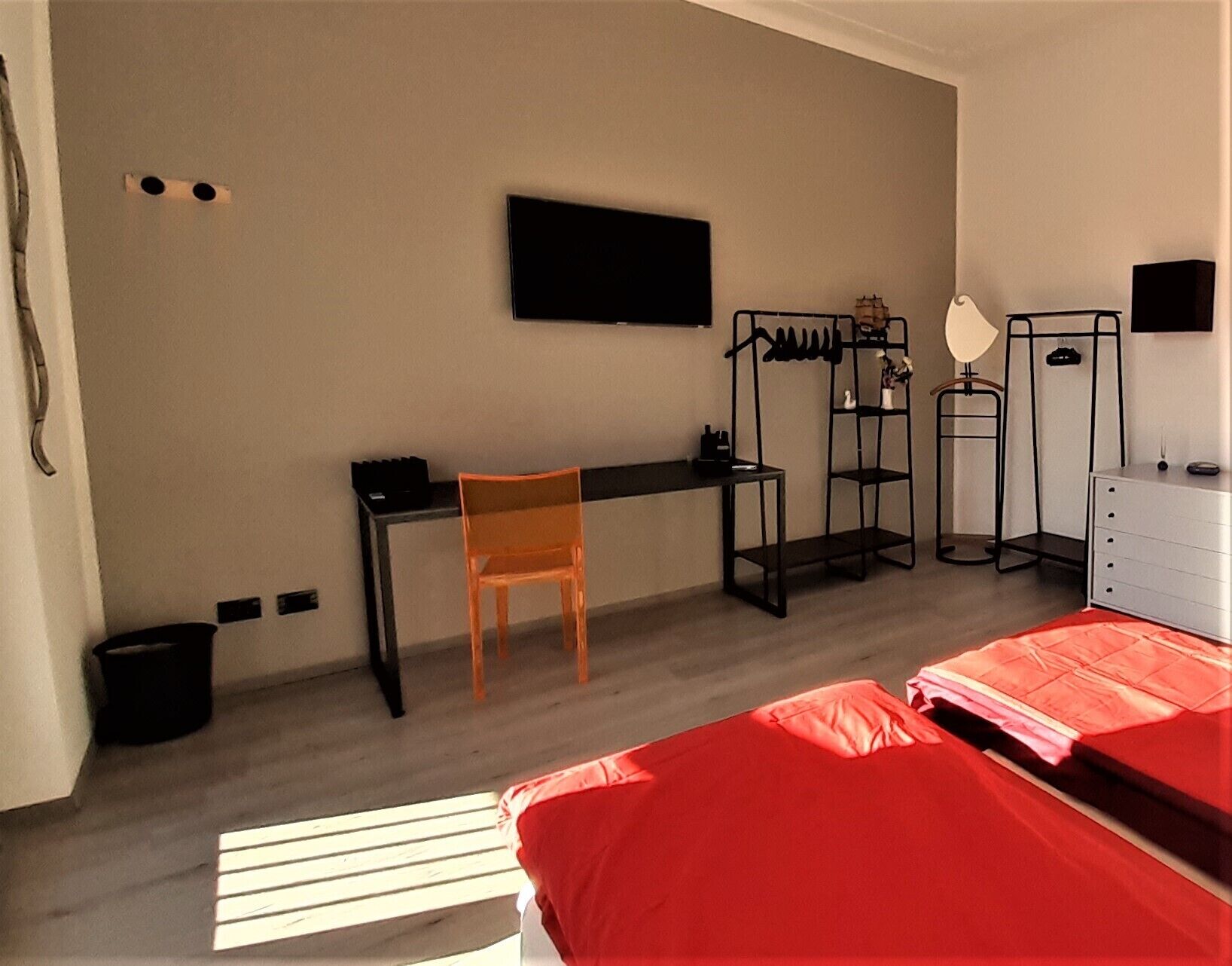 A bedroom with a bed, a desk, a chair, a TV, a wardrobe, and a small trash bin.