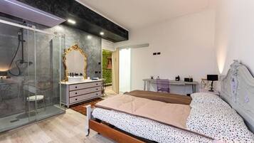Een moderne slaapkamer met een glazen douche, een wastafel met gouden spiegel, een bed met een bedovertrek met dessin en een bureau met stoel.