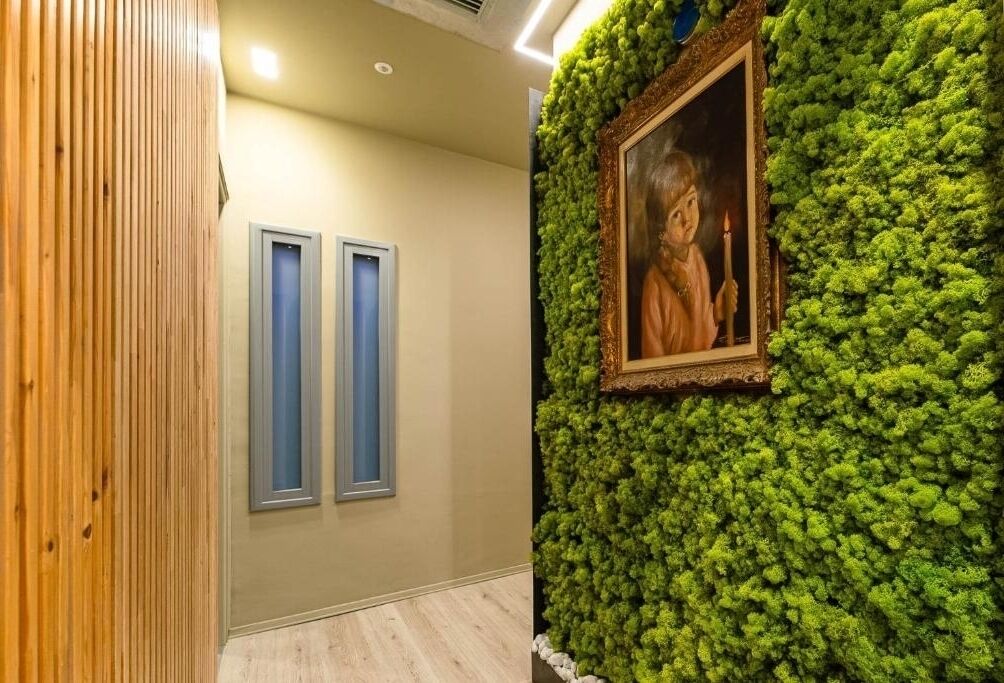 Ein Korridor mit Holzwandverkleidung, zwei blauen Türrahmen und einer Wand, die mit Grünpflanzen und einem gerahmten Porträt bedeckt ist.