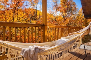 A hammock on a wooden deck with a view of autumn foliage.