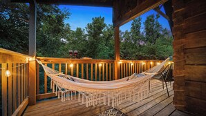 Una terraza de madera con una hamaca, luces colgantes y vista a árboles.