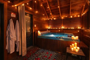 A wooden spa room with a hot tub, candles, and towels.