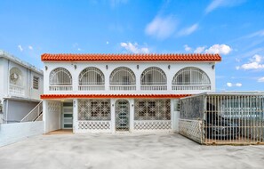 A two-story building with a red-tiled roof, white walls, and multiple arched windows with metal grilles.