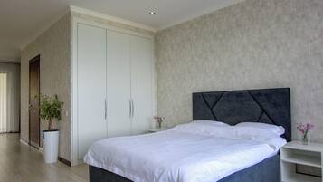 A modern bedroom with a large bed, a wardrobe, and a potted plant.