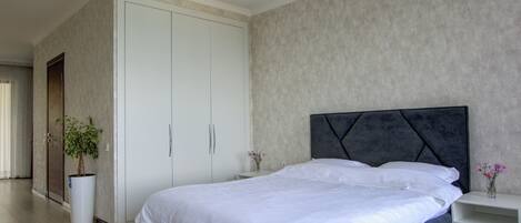 A modern bedroom with a large bed, a wardrobe, and a potted plant.