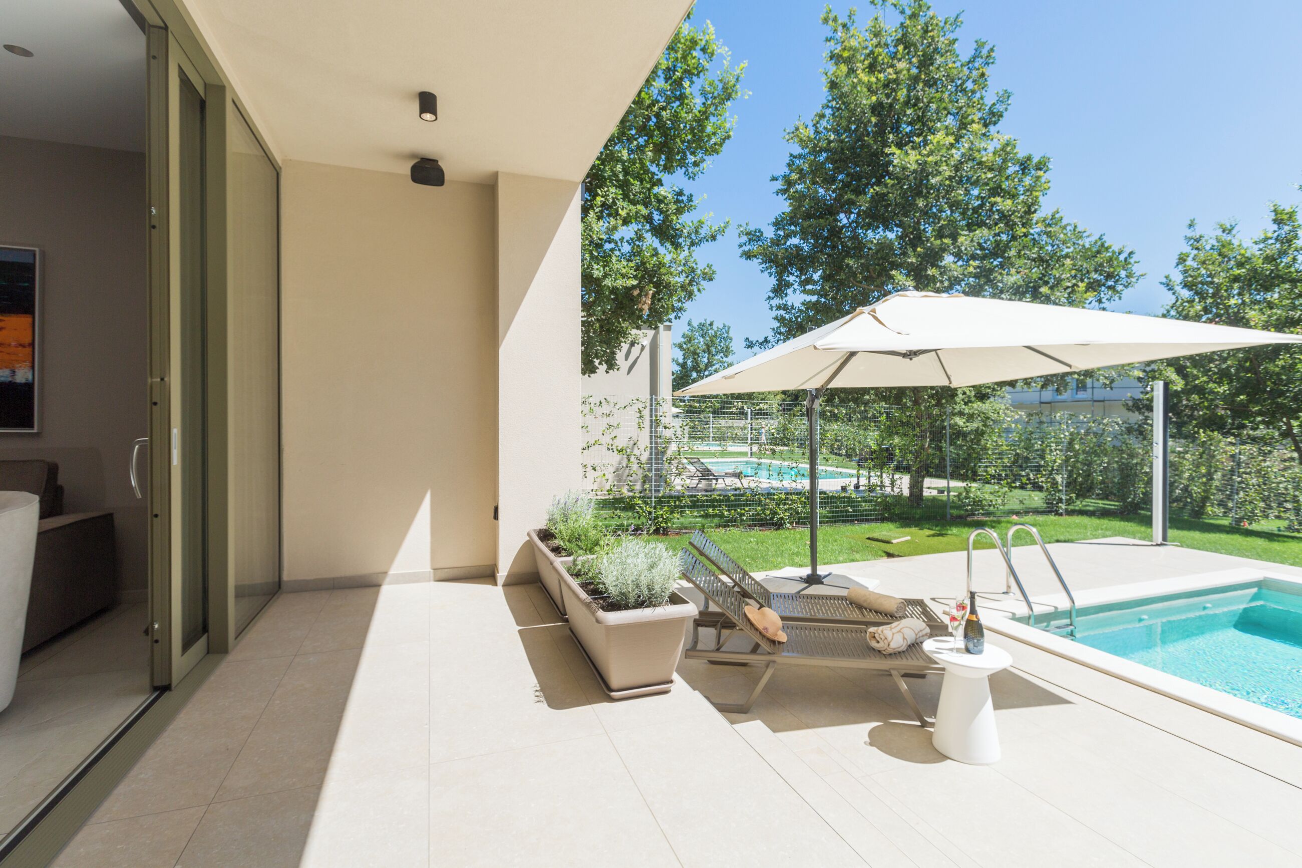 A modern outdoor pool area with a lounge chair, umbrella, and potted plants.