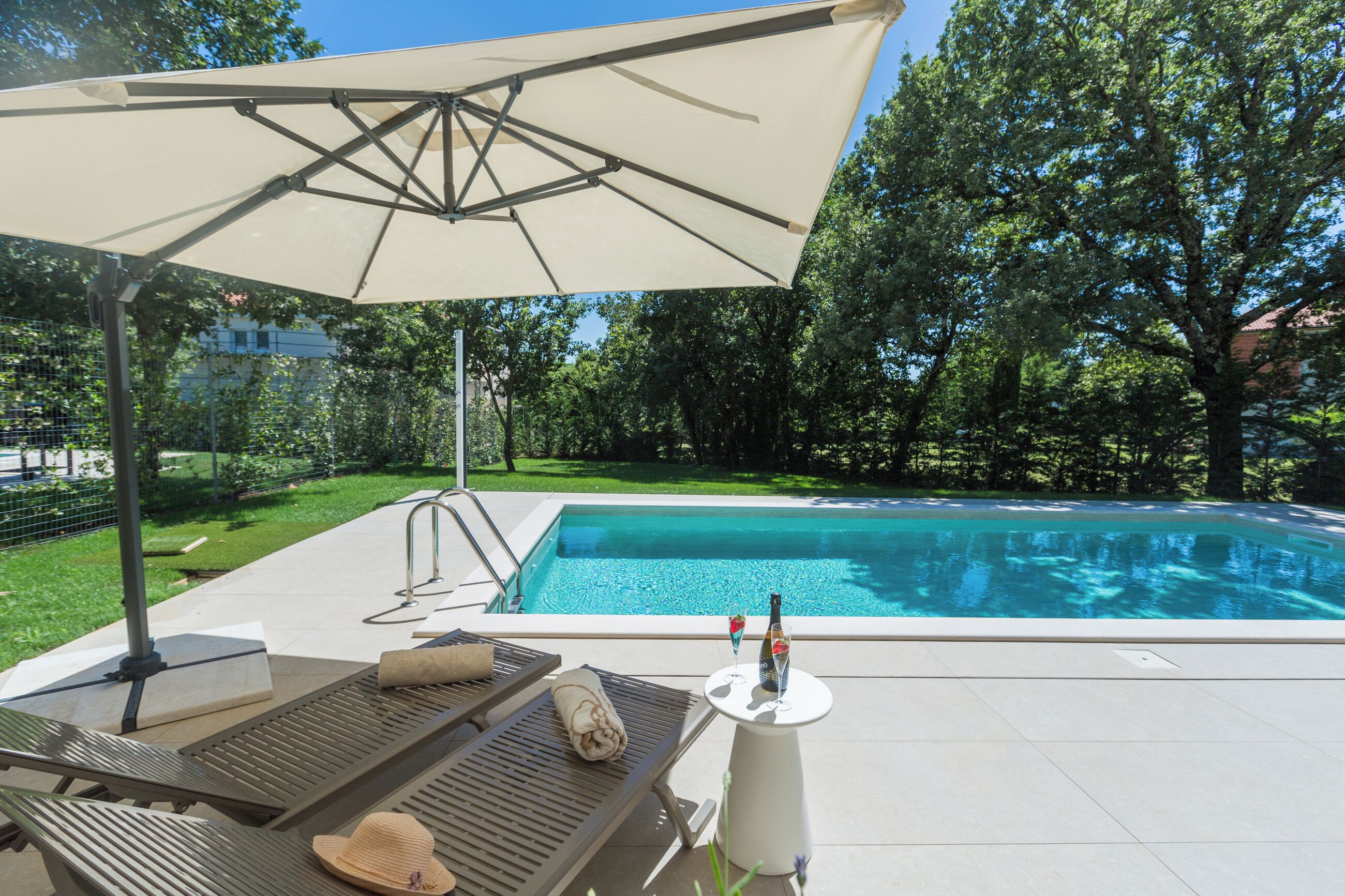 Un espace aménagé au bord de la piscine, avec un fauteuil de relaxation, un parasol et une bouteille de champagne.