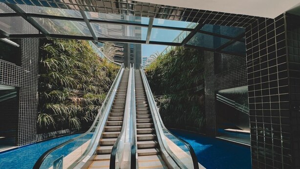 An indoor pool area with an escalator leading to a higher level. - Landscape Torre Platinum (Fortaleza)