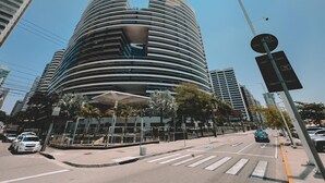 A modern, multi-story building with a curved facade, surrounded by palm trees and other urban infrastructure. - Landscape Torre Platinum (Fortaleza)
