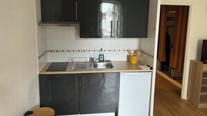 A compact kitchen with black cabinets, a white dishwasher, and a tiled backsplash. - Apartment historic center Monségur (Monségur)
