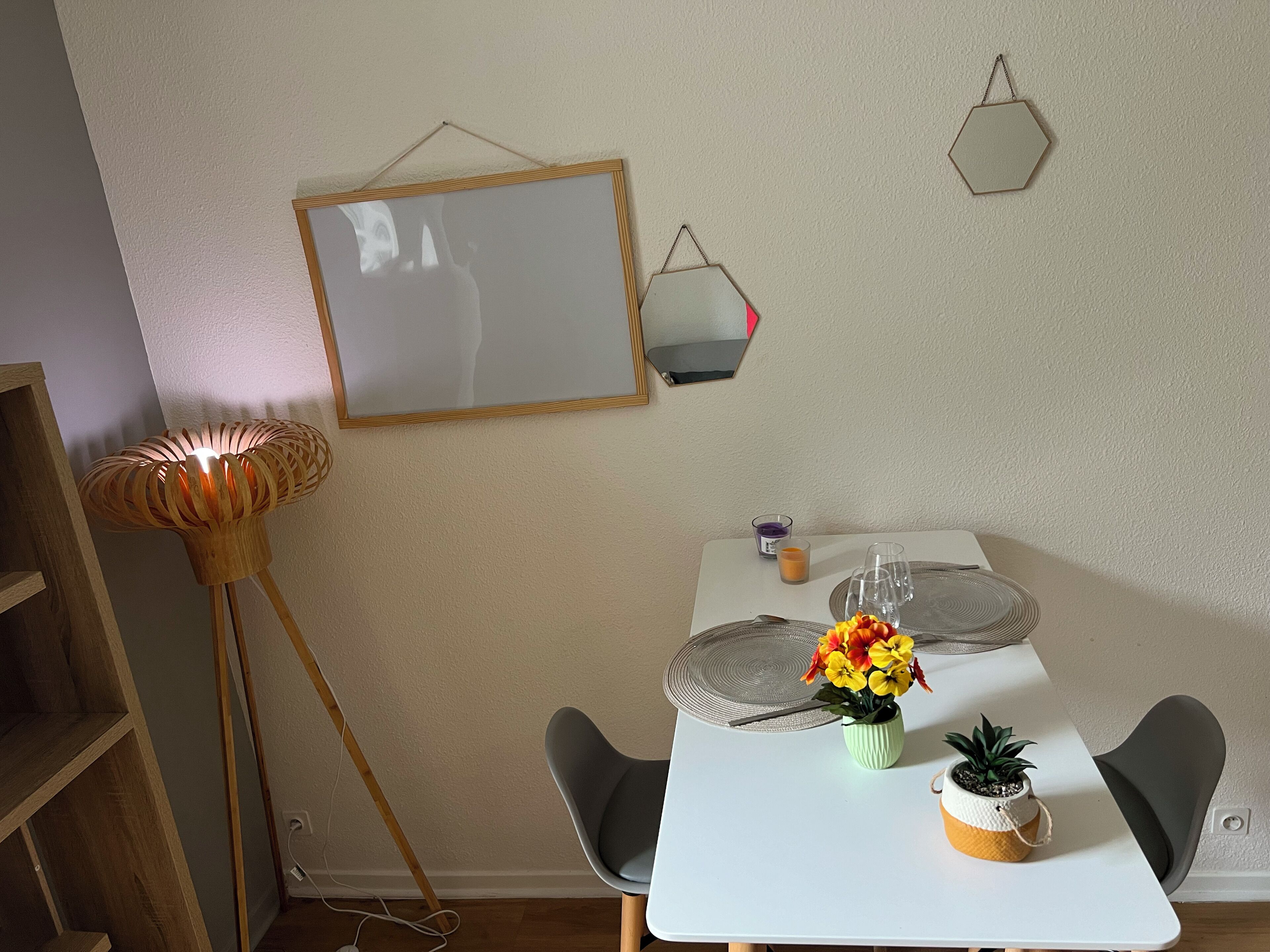 Un coin repas avec une table blanche, deux chaises, un lampadaire et un miroir au mur.