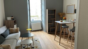 A modern living room with a sofa, a small table, and a dining area with chairs. - Apartment historic center Monségur (Monségur)